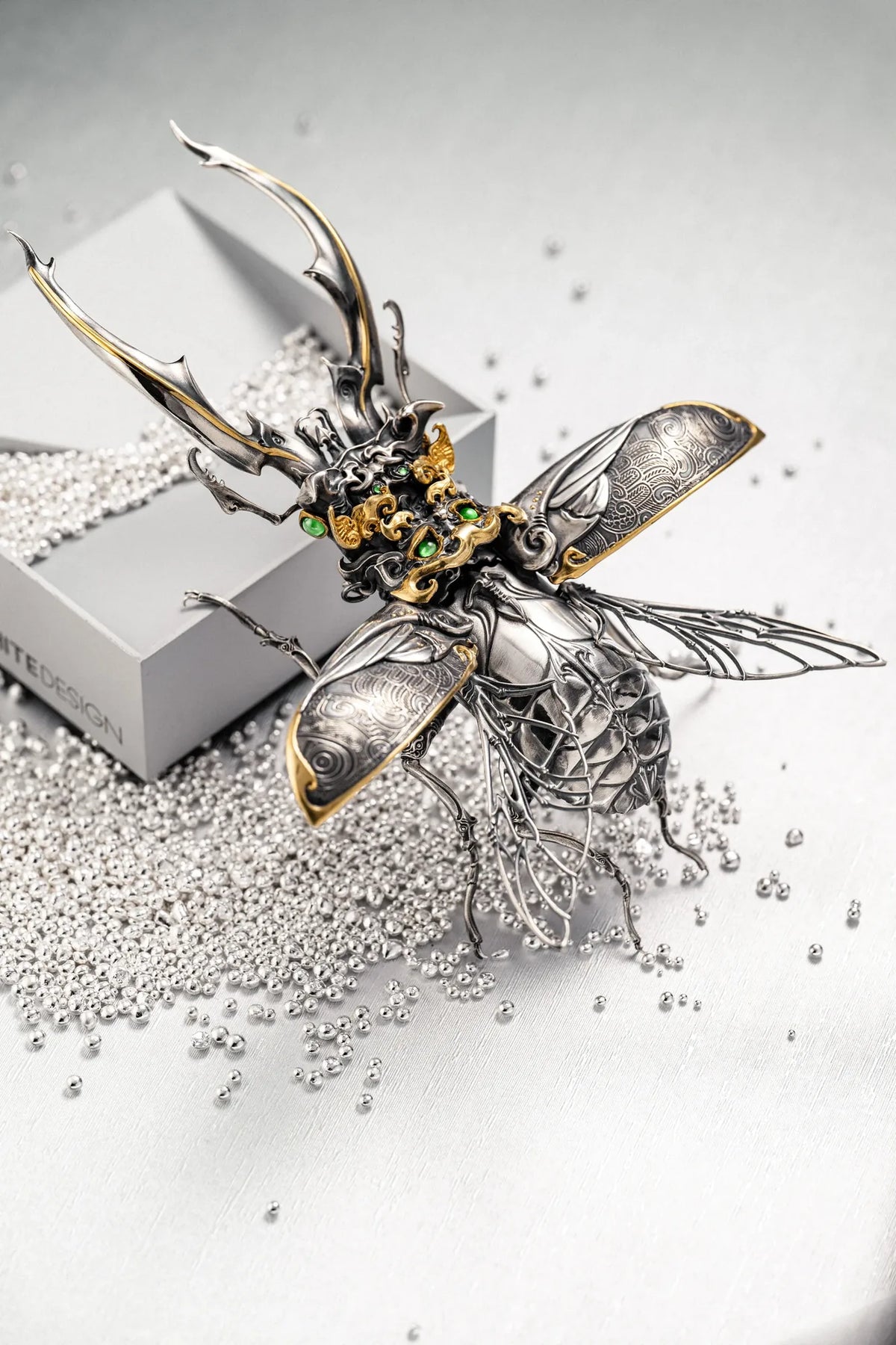 Ghostface Beetle in a silver finish with its wings spread, beside silver-colored granules