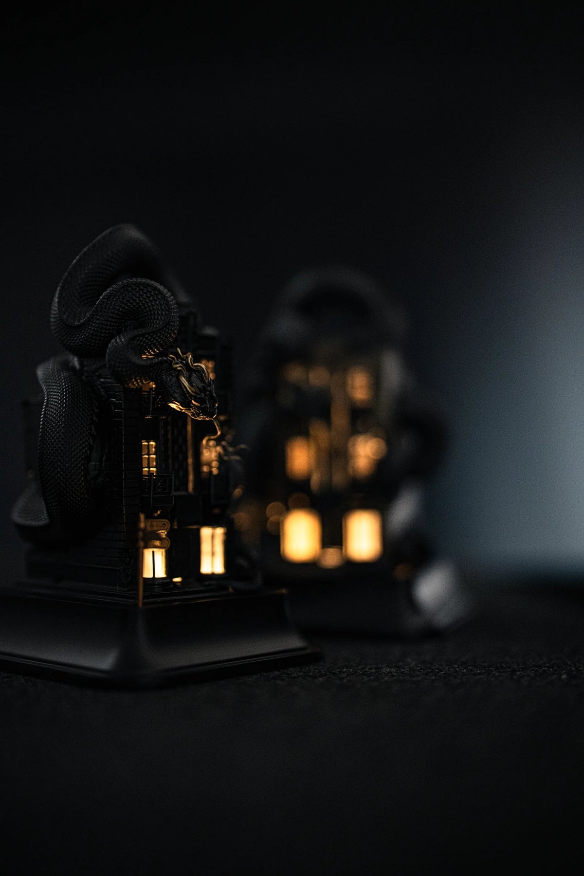 Two WUYIN x NOCAL:LOWCAL serpent house sculptures with illuminated windows in a dark setting.