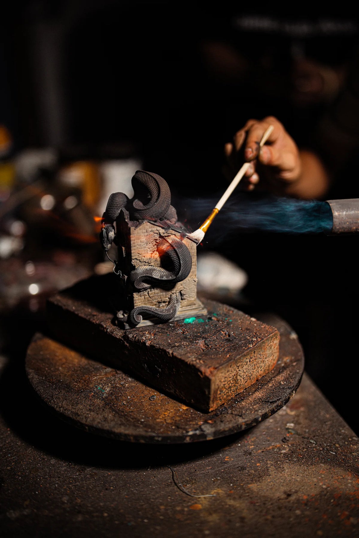 A craftsperson applies a finish to the WUYIN x NOCAL:LOWCAL serpent house sculpture during heating.